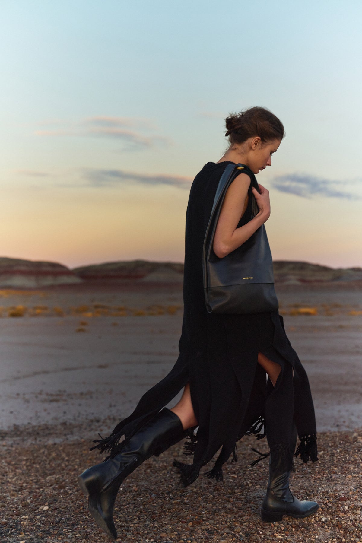 Model walking through a rocky landscape with The Collector tote in Black leather and Gold hardware