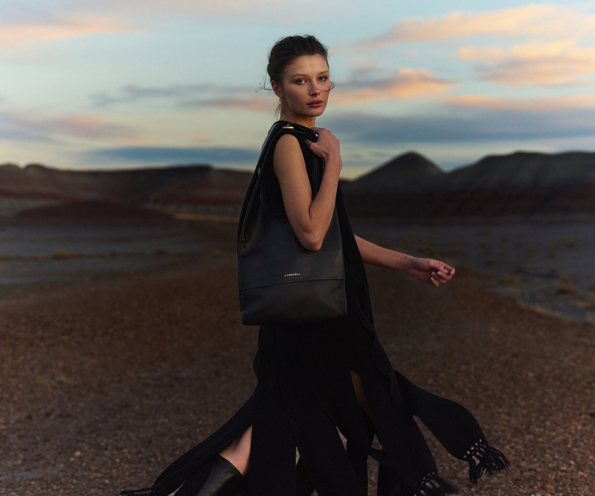Model carrying The Collector tote in Black leather and Gold hardware at sunset