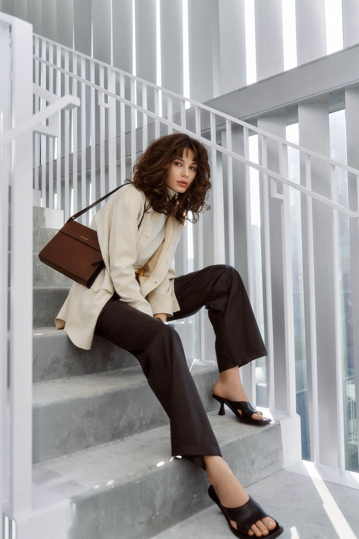 Model seated on steps wearing the Low Rise bag in Cacao leather