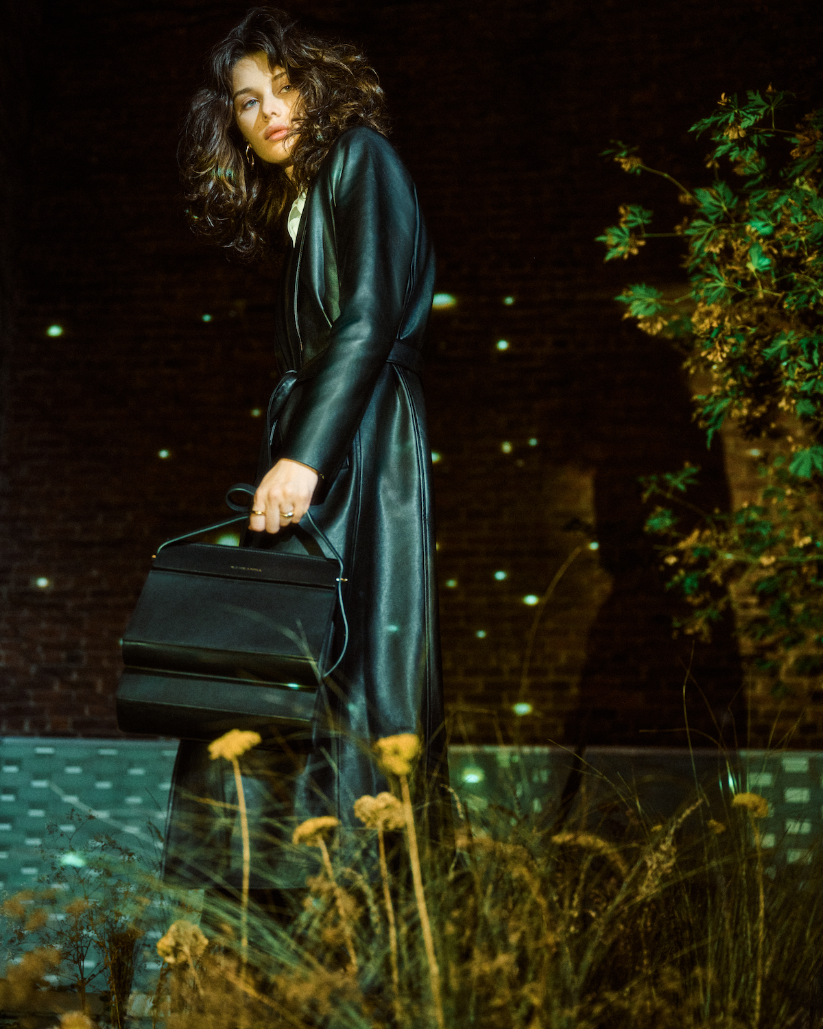 Model carrying the High Rise bag in Black leather in a garden
