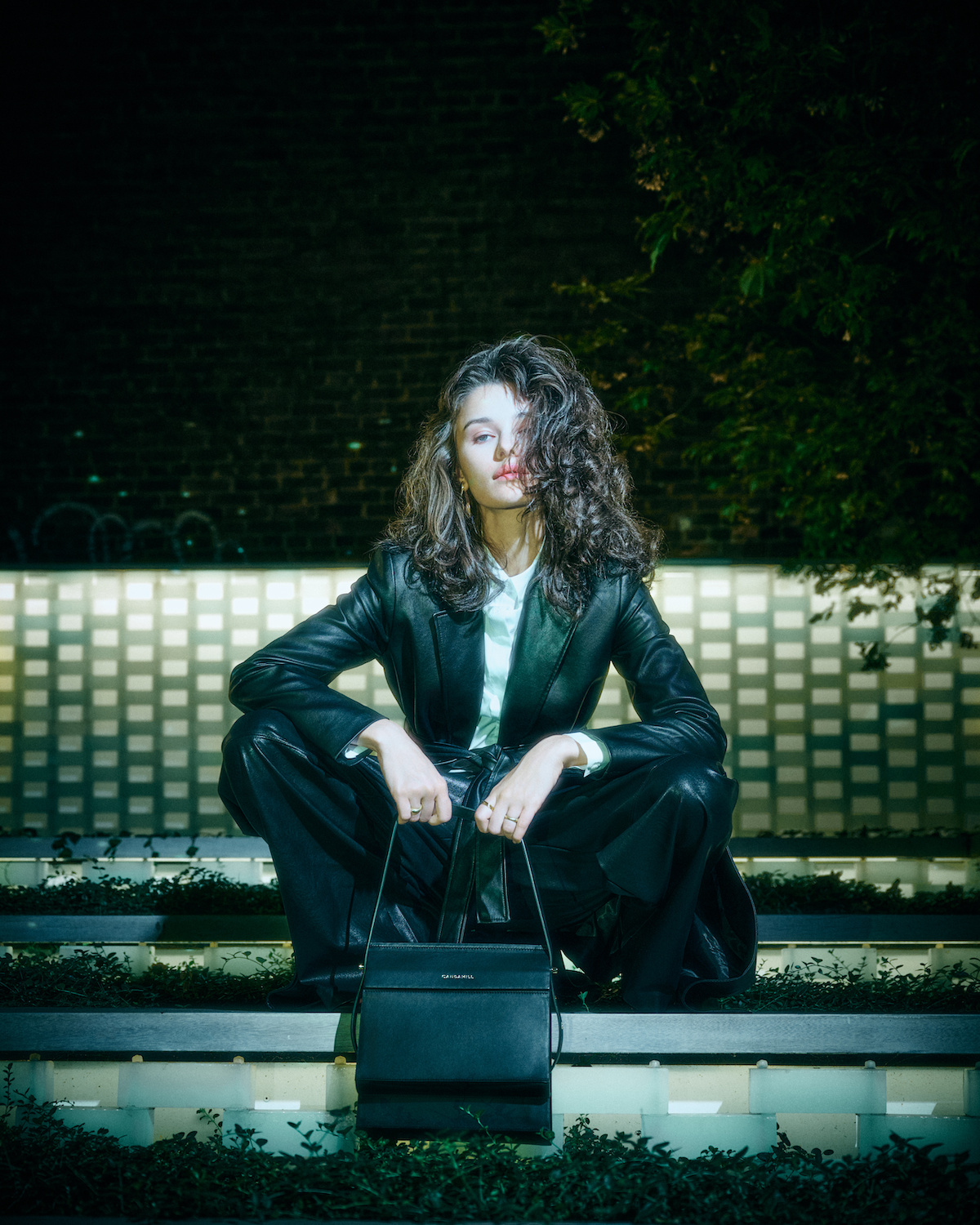 Model seated on a tiled bench with the High Rise bag in Black leather