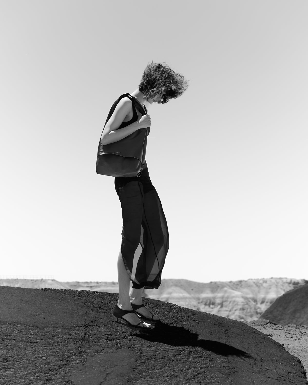 Black-and-white photograph of a model carrying The Collector Silver tote on a rocky ridge