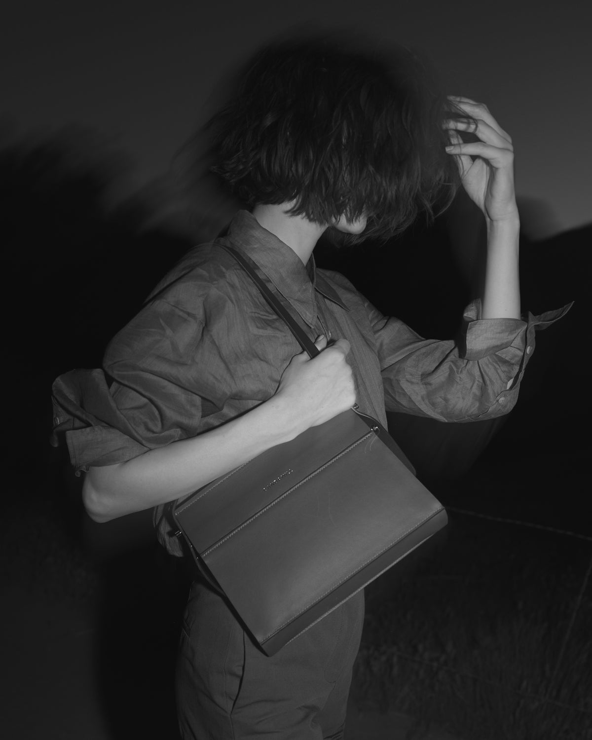 Black-and-white portrait of a model holding the Low Rise bag in Saddle