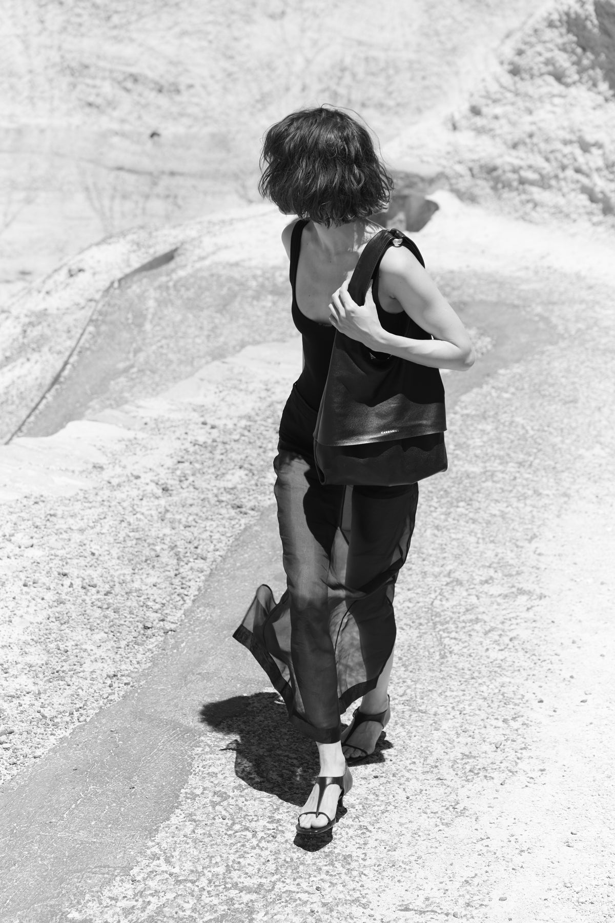 Black-and-white photograph of a model wearing The Collector Silver tote among rocks